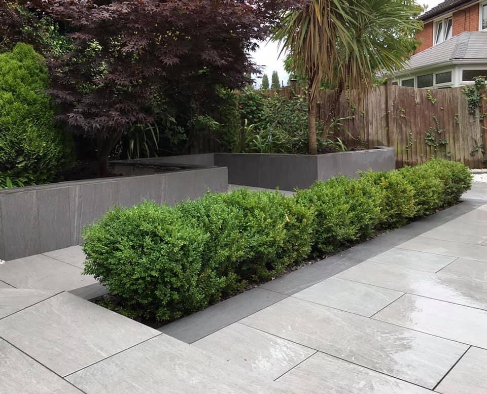 Grey paved steps and raised planters around a clipped hedge