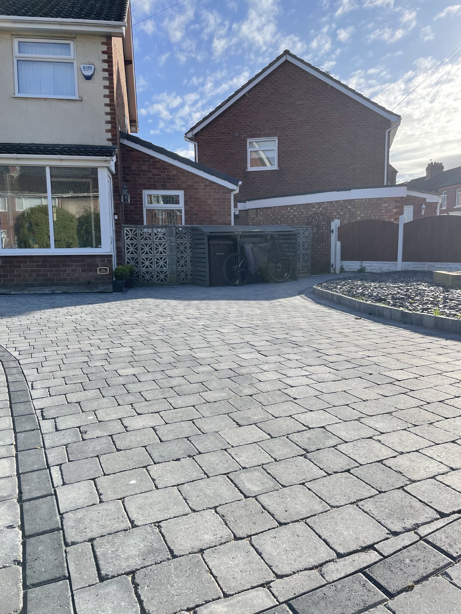 A grey cobble-style block driveway curving past a house