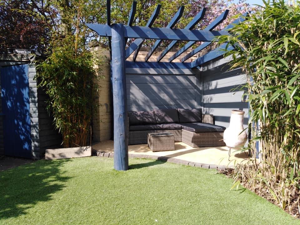 A pergola seating corner beside artificial grass and tall planting